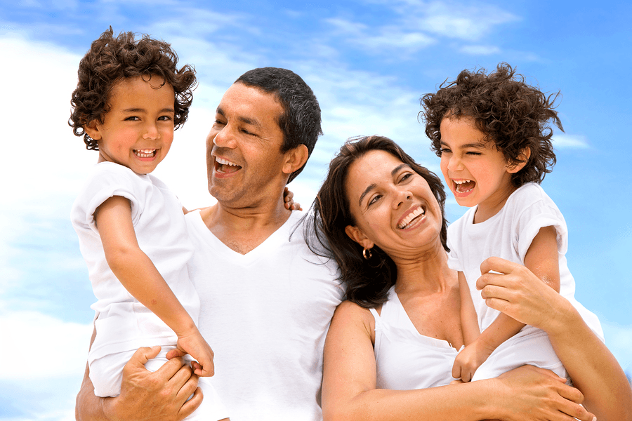 A happy family of four laughing together under a bright blue sky