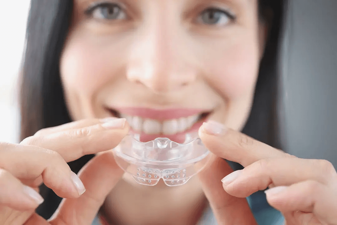 Smiling patient holding a clear custom-fitted mouthguard up to her teeth